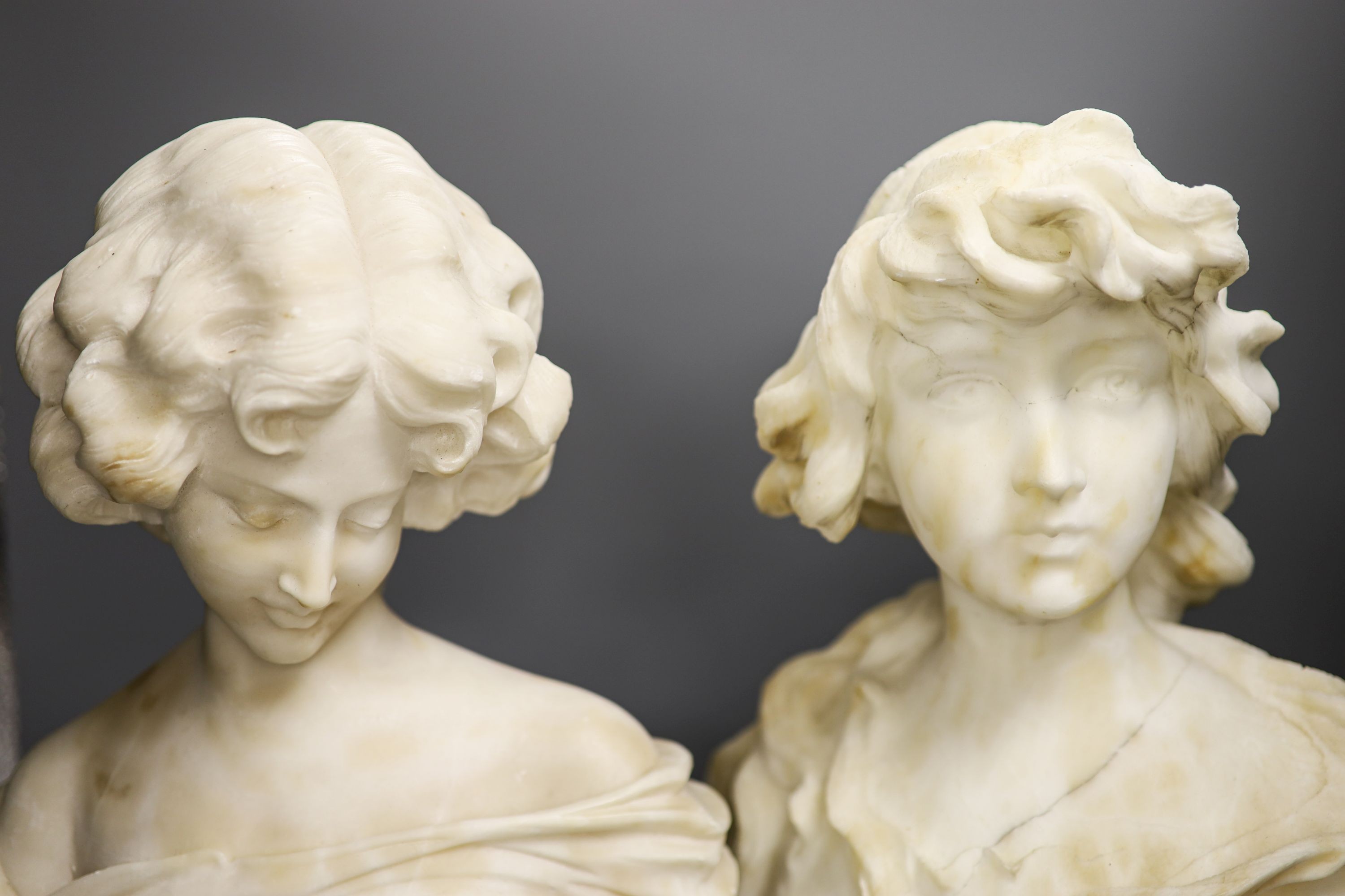 Two white alabaster busts of young women, raised on turned plinths 44cm